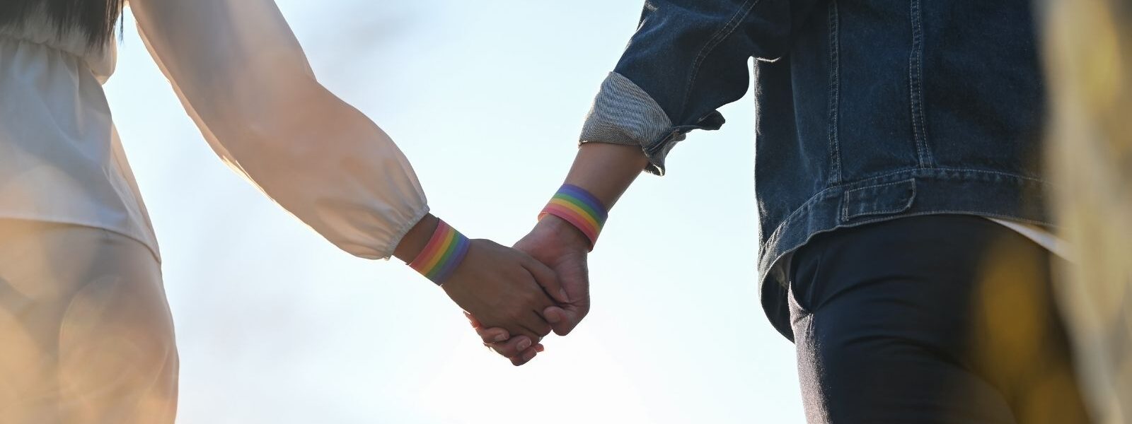 A zoomed in photo of a couple holding hands wearing paper rainbow wristbands signifying they are in support of the LGBT community
